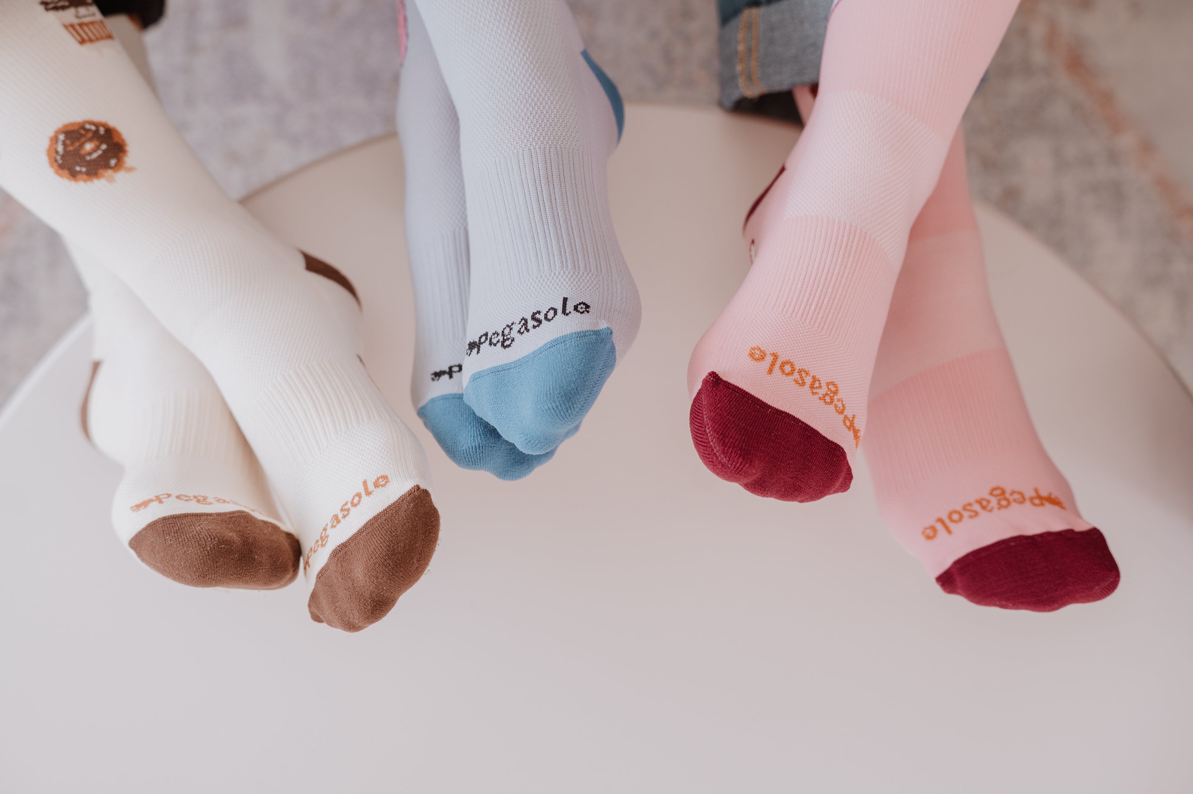 Three pairs of feet wearing Pegasole Compression socks on white table.