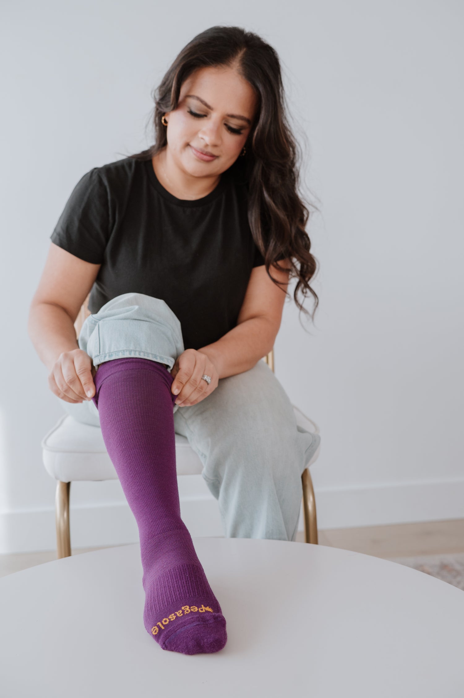 Woman sitting on a chair wearing a black t-shirt and Pulling up Pegasole Compression socks.