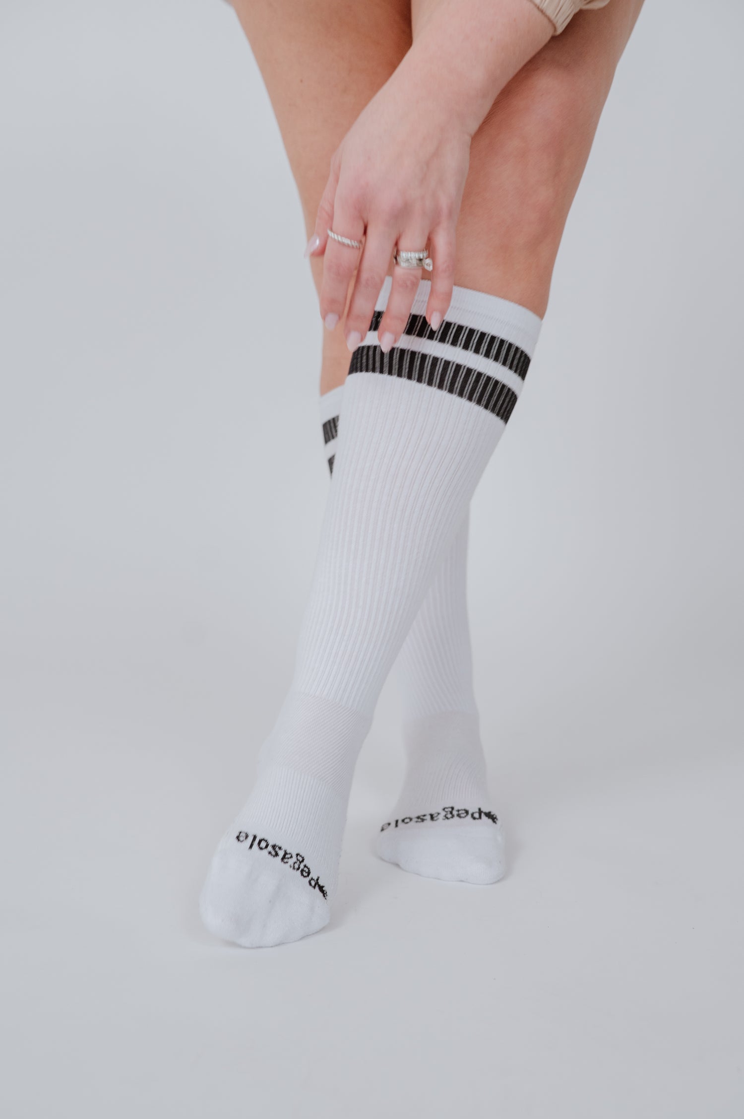 Woman wearing white pegasole compression socks with black stripes and on a light gray background