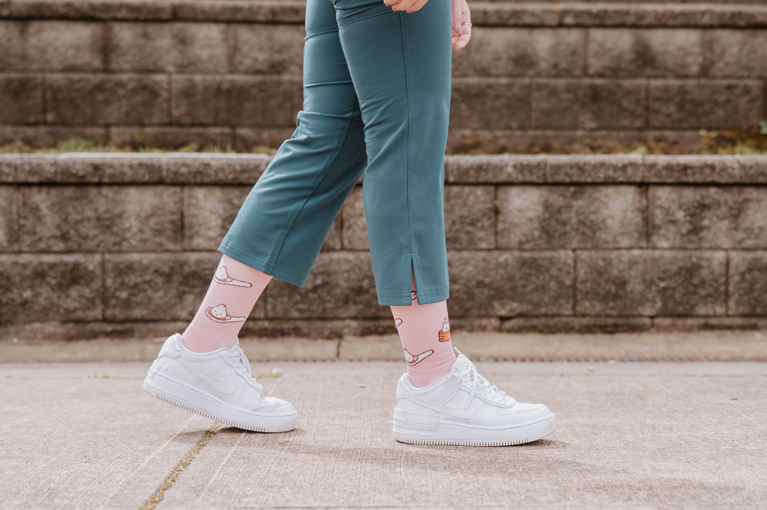 Person wearing teal pants and white sneakers with Pegasole Compression Socks on a concrete surface with a stone wall background